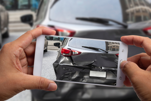 Person photographing rear-end vehicle property damage on a car after an accident.