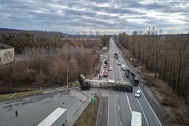 An overturned semi-truck is blocking the intersection after wide-turn truck accidents, causing major traffic disruption and potential injuries.